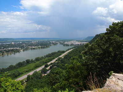 [Looking down approximately 500 feet to the roadway and lake below. The edge of the bluff is seen at the right and in the distance beside it are dark clouds extending down to the ground.]